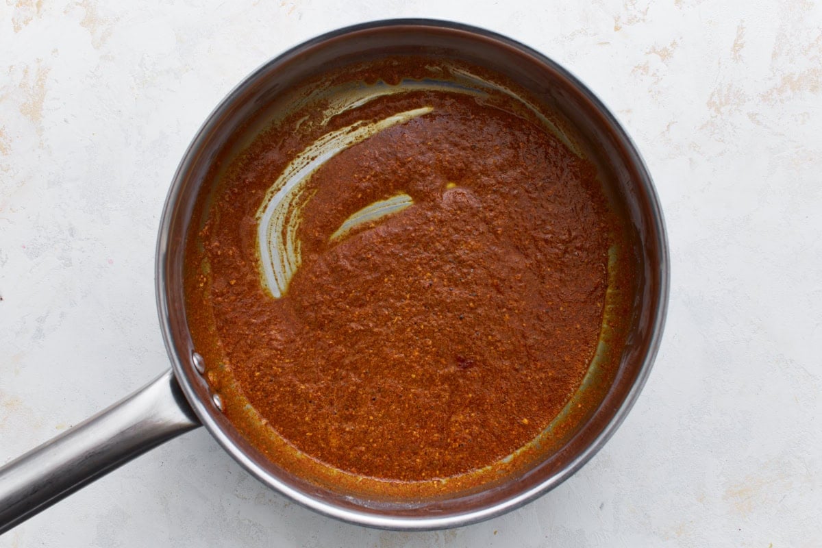 Spices blended into the roux in a saucepan, creating a thick, reddish-brown paste.