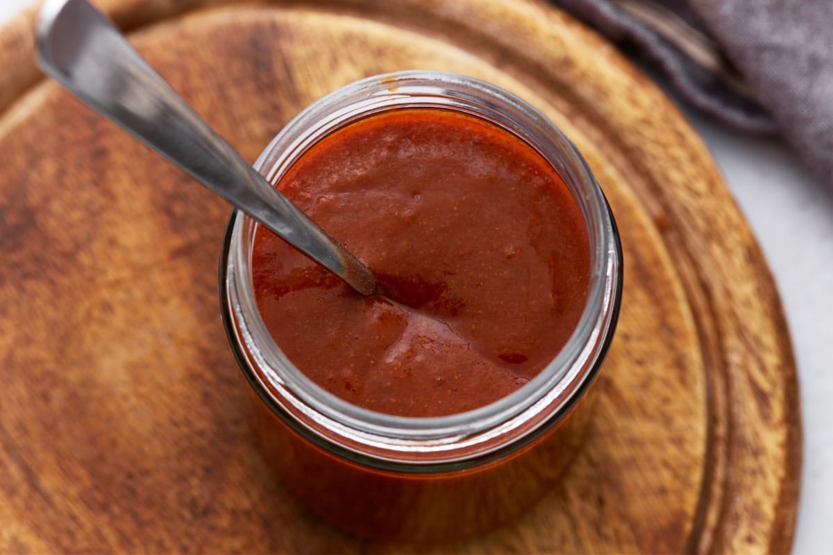 Top-down view of a jar filled with thick enchilada sauce, with a spoon dipped inside.