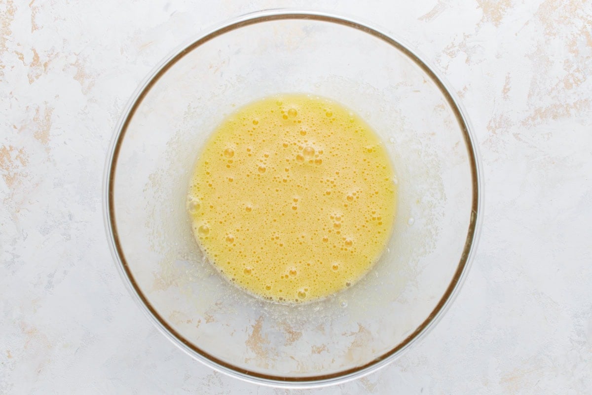 Whisked eggs and sugar in a clear glass bowl, lightly frothy and pale yellow.
