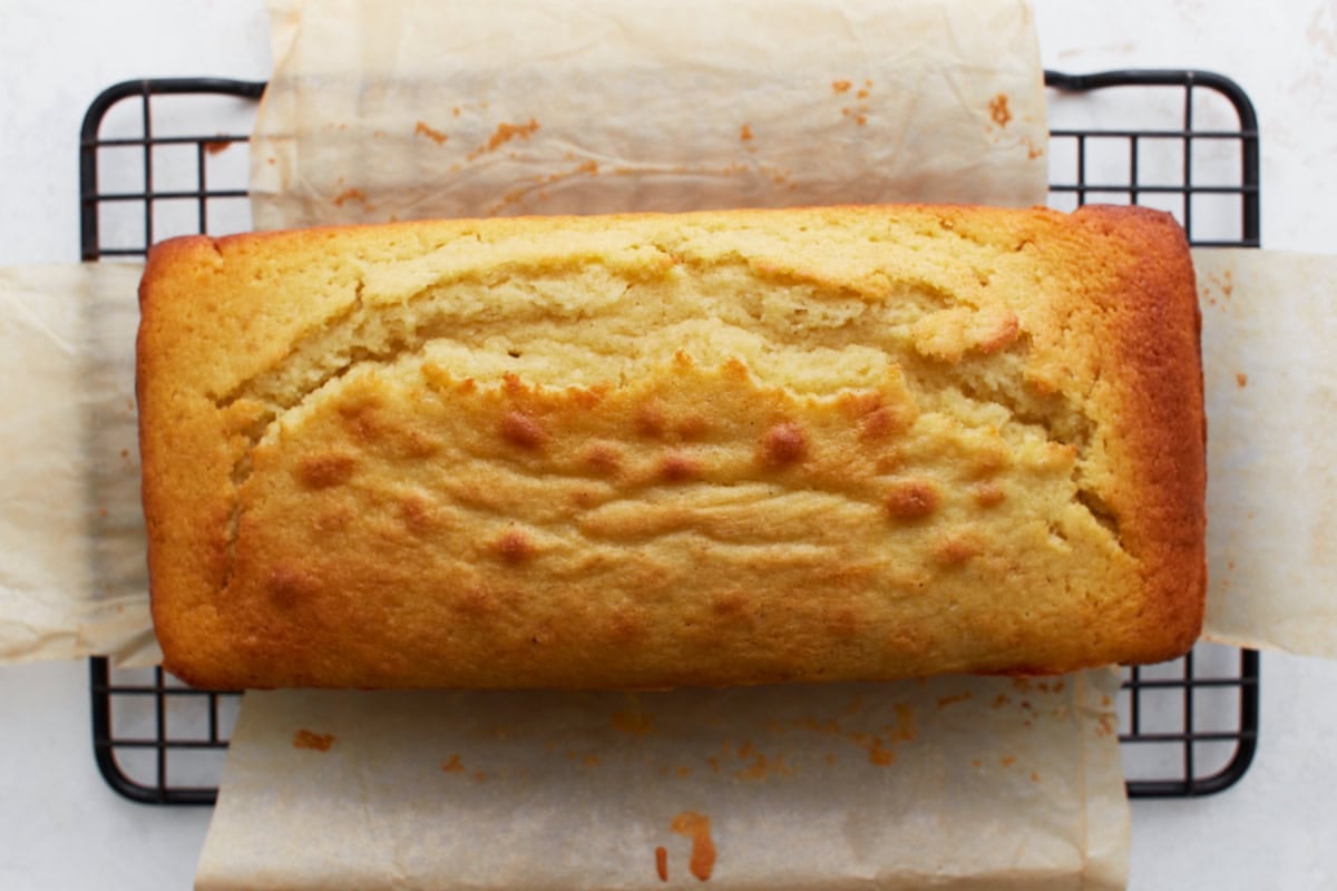 Baked lemon loaf cooling on a wire rack with parchment paper underneath.
