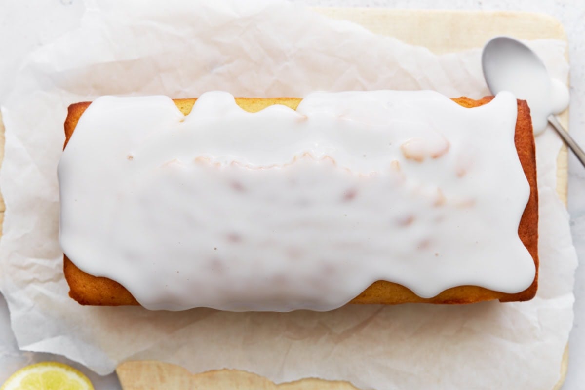 Iced lemon loaf on parchment paper with glaze spread evenly over the top.