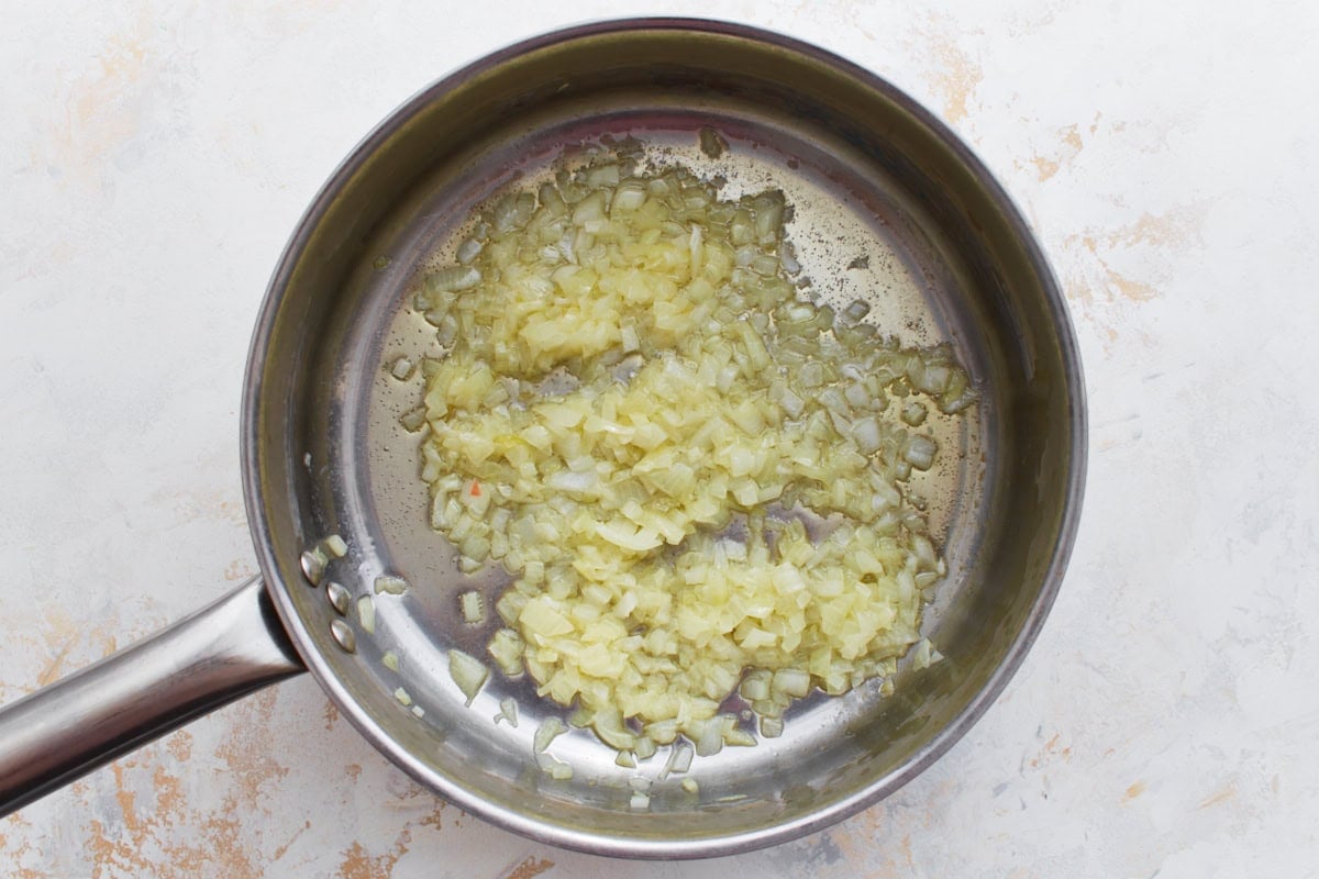 Finely chopped onions sautéing in olive oil in a stainless steel pan.