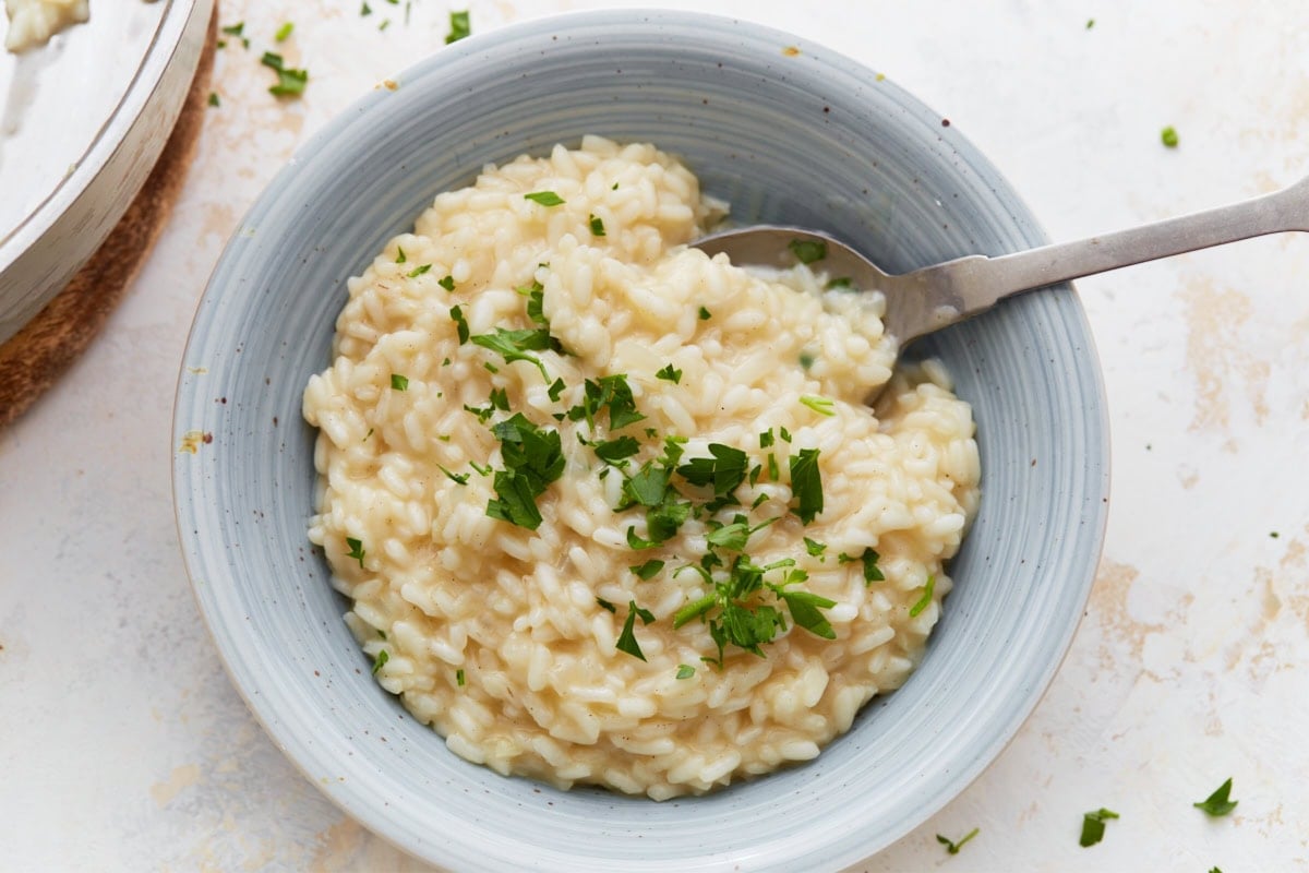 Bowl of creamy gluten-free risotto topped with chopped parsley, served with a spoon in a light blue dish.