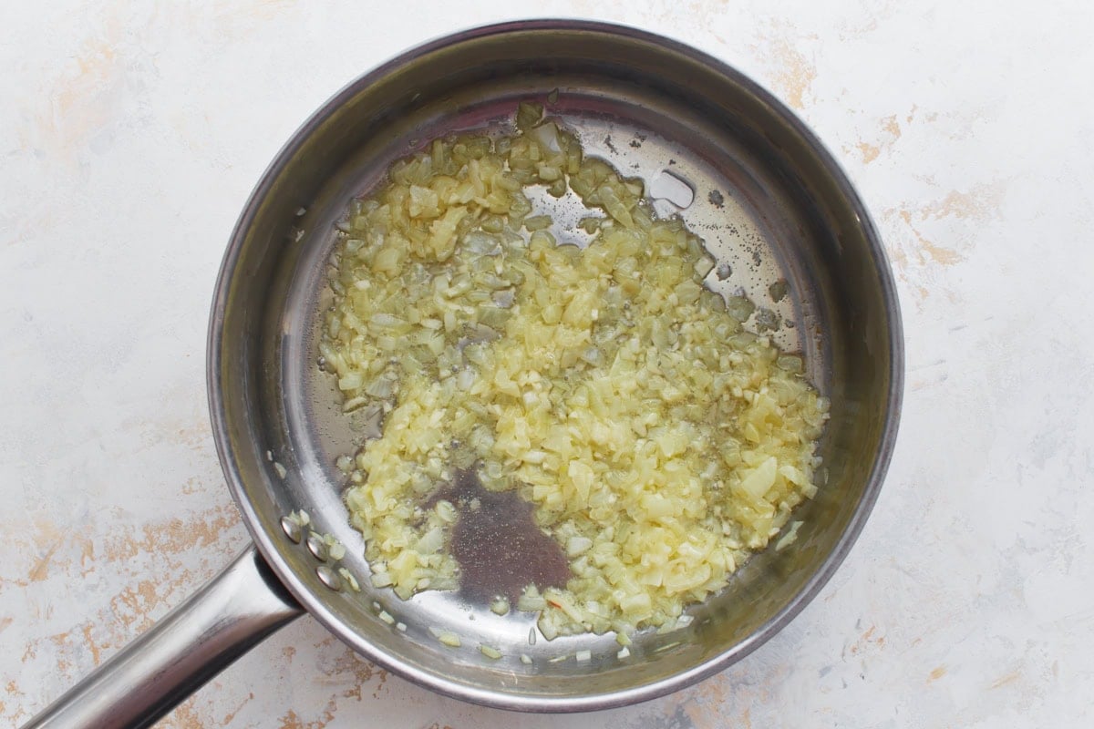 Onion and garlic mixture cooking down and softening in a pan.