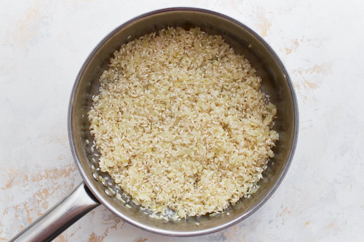 Arborio rice added to the pan with onions, ready to toast.
