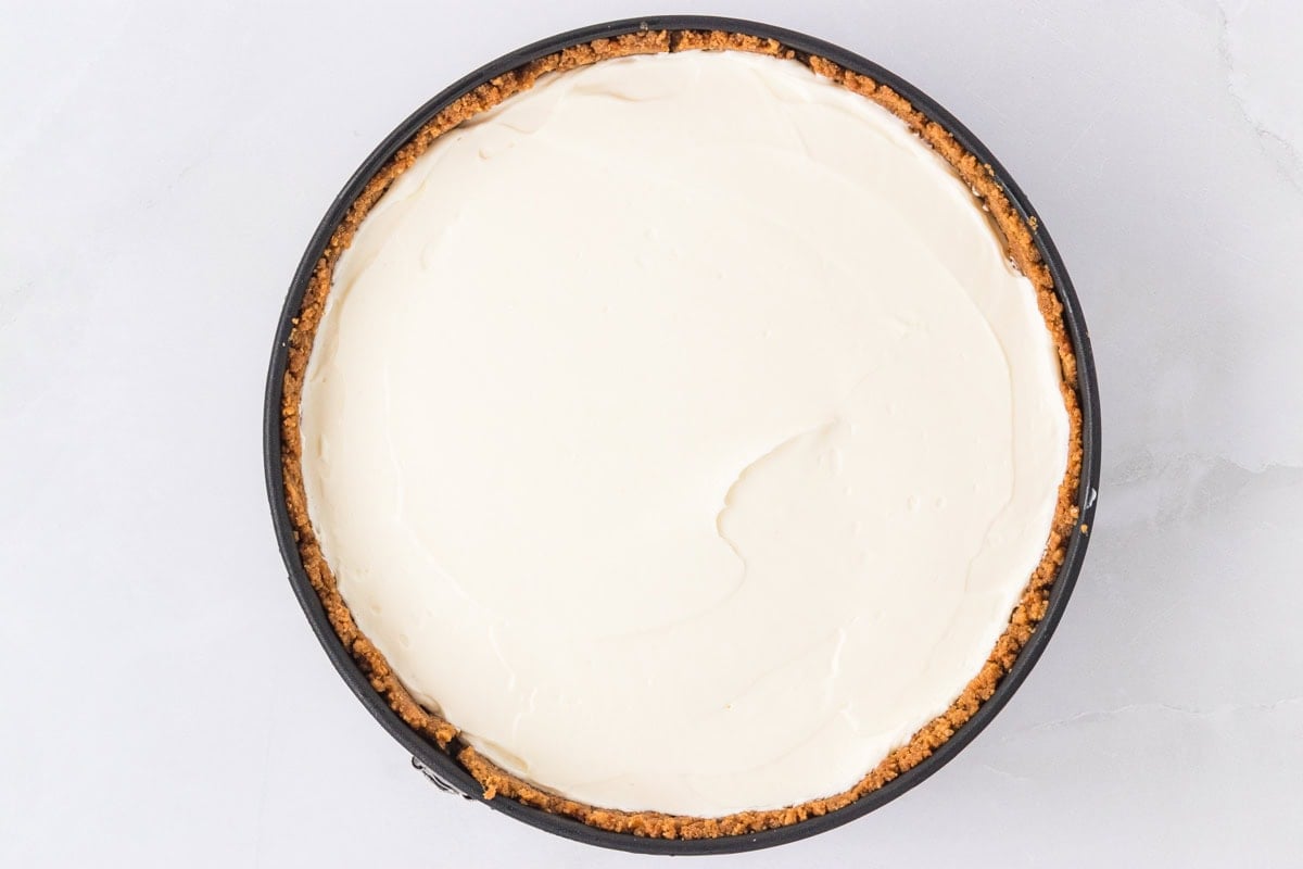No-bake cheesecake filling spread evenly in the prepared graham cracker crust in a springform pan, ready to chill.