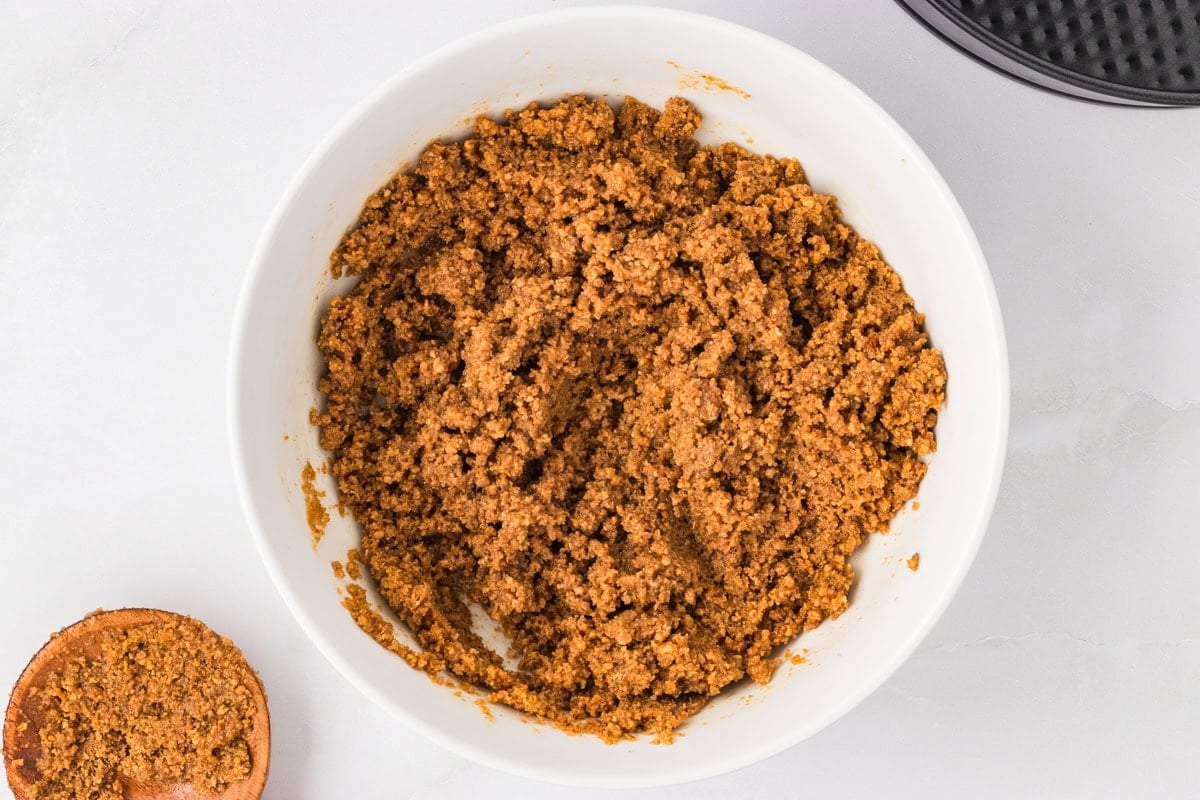 A white bowl filled with mixed gluten-free graham cracker crust crumbs ready to be pressed into a pan.