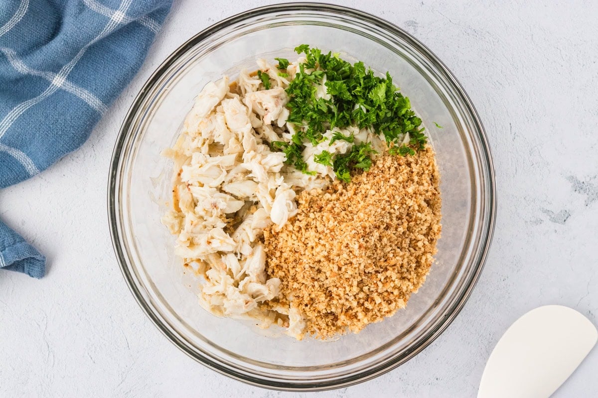 A bowl of lump crab meat, chopped parsley, and gluten-free breadcrumbs before being mixed together.