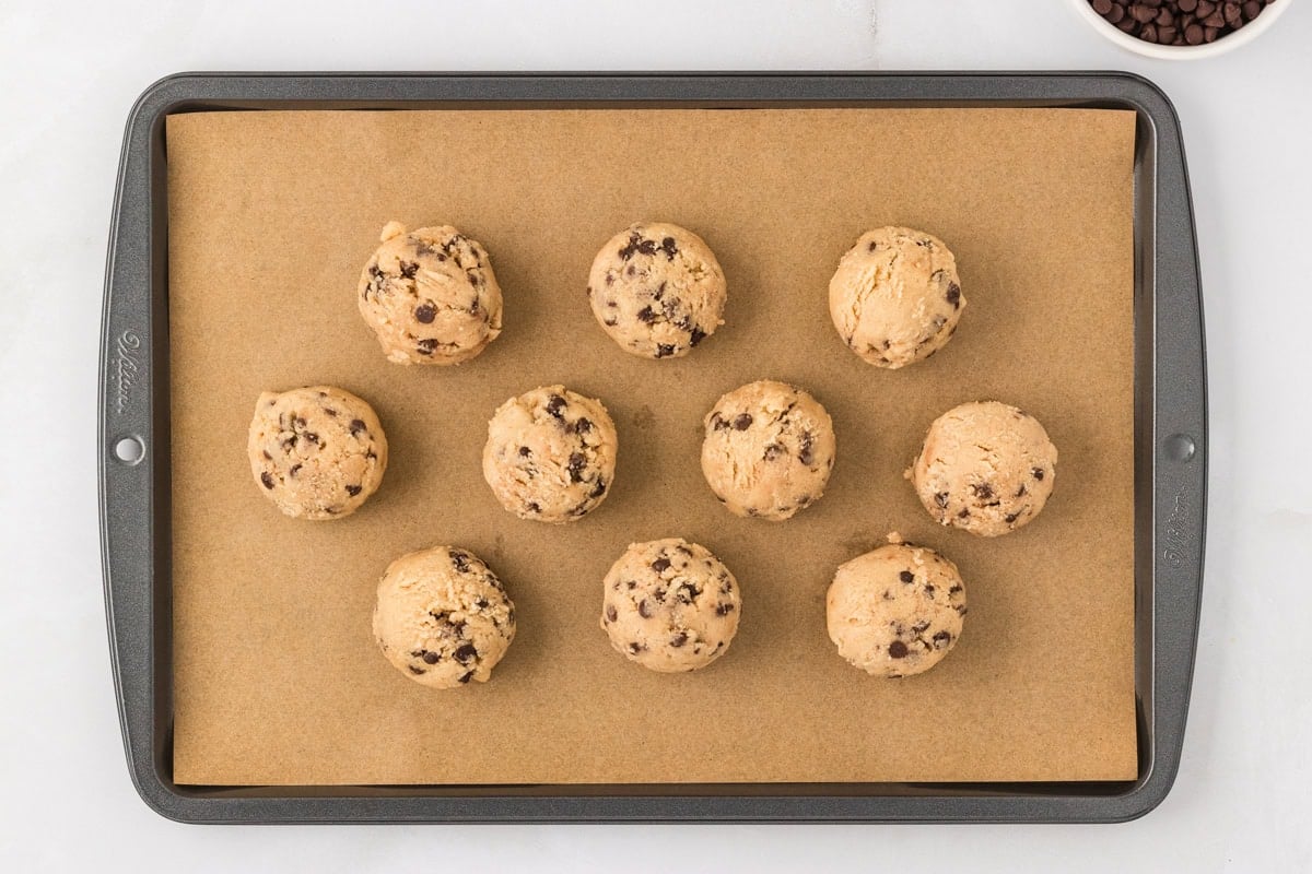Scoops of gluten-free edible cookie dough arranged on a parchment-lined baking sheet.