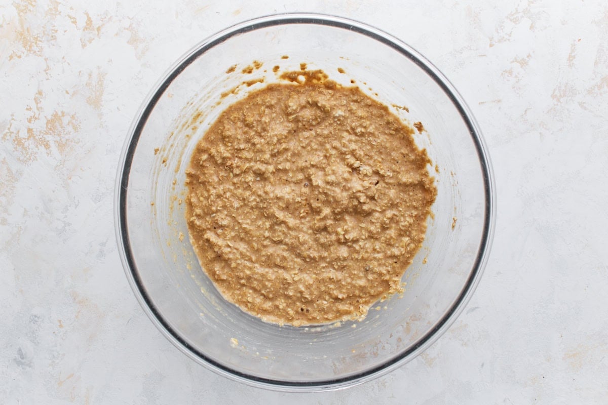 Wet and dry ingredients combined into a thick, textured oatmeal batter in a glass mixing bowl.