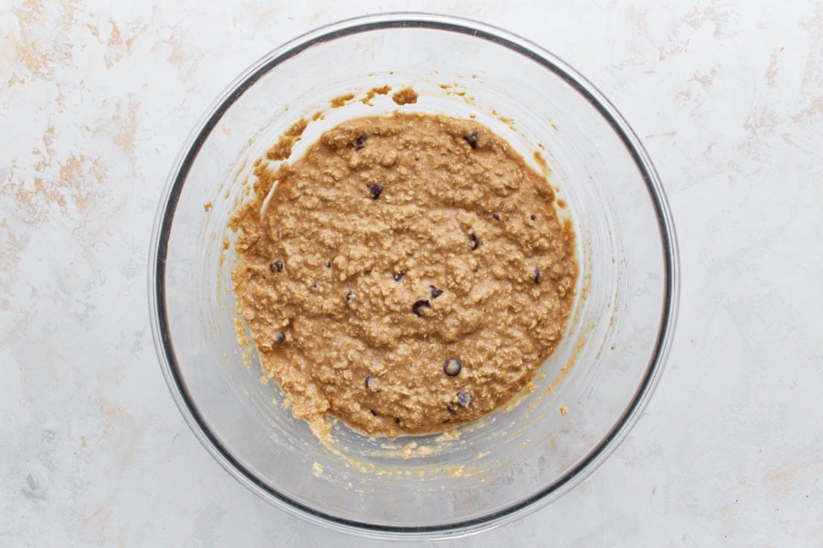 Oatmeal bar batter with chocolate chips stirred in, shown in a large glass bowl.