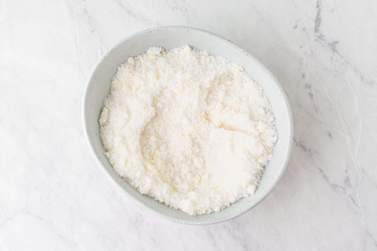 Granulated sugar mixed with lemon zest in a white bowl, showing a fragrant and slightly damp texture.