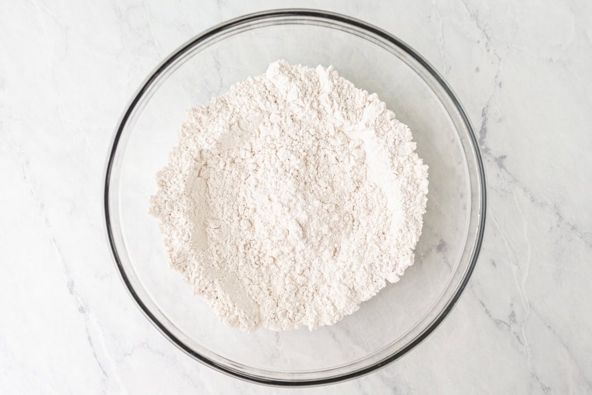 Dry ingredients including gluten-free flour, baking powder, baking soda, and salt mixed together in a clear glass bowl.