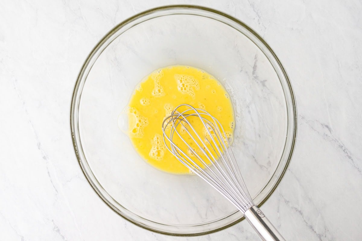 Whisked eggs in a glass bowl with a metal whisk resting inside.