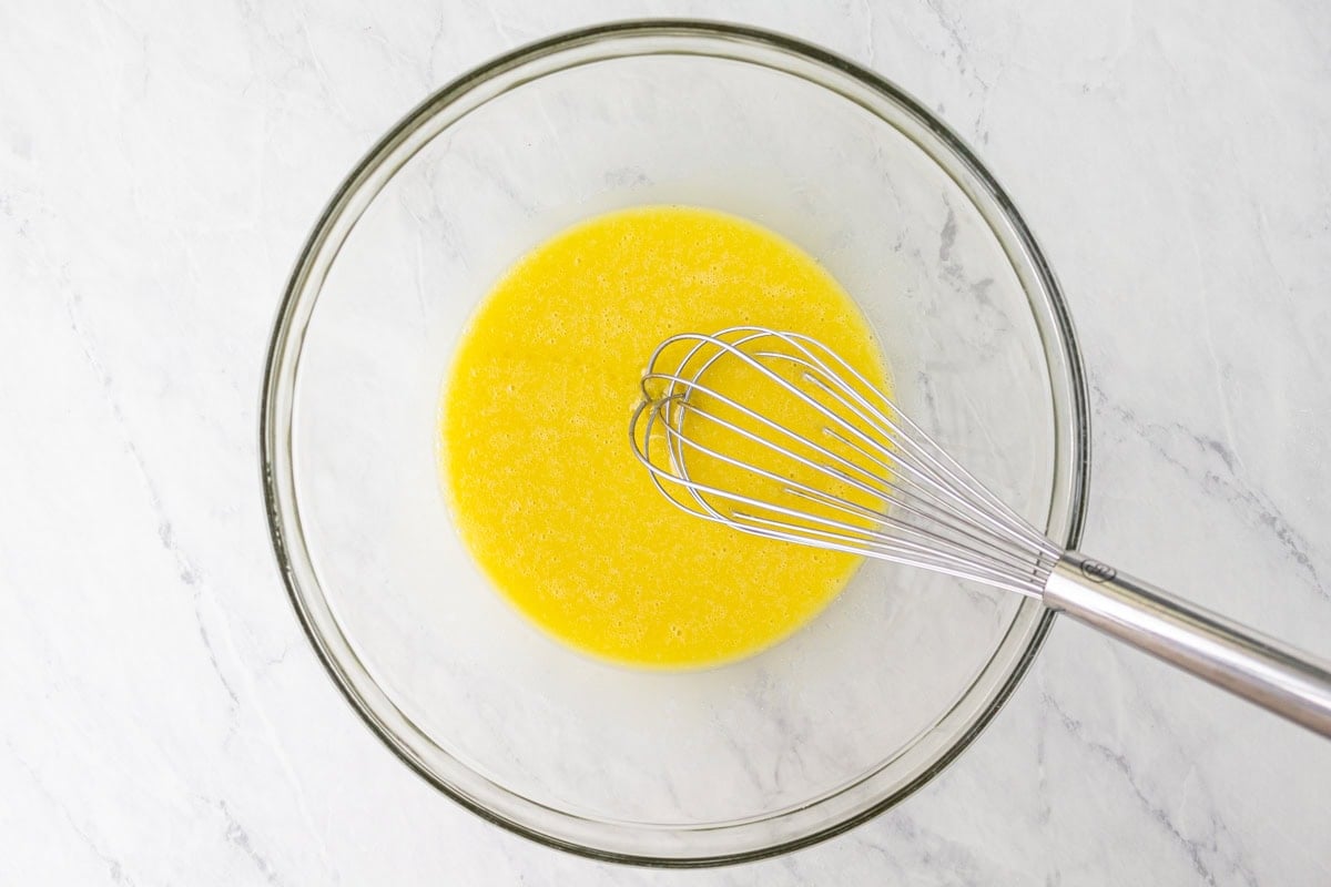 Eggs and olive oil whisked together in a glass bowl, forming a smooth and emulsified mixture.