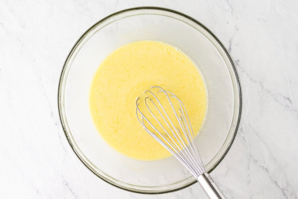 Wet ingredients fully mixed into a smooth yellow batter in a glass bowl.