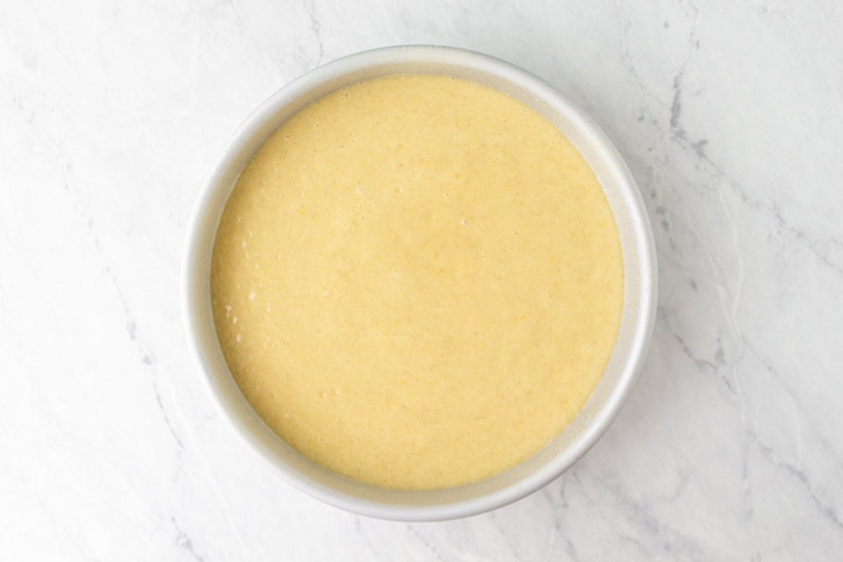 Completed cake batter poured into a round metal cake pan, smooth and ready for baking.