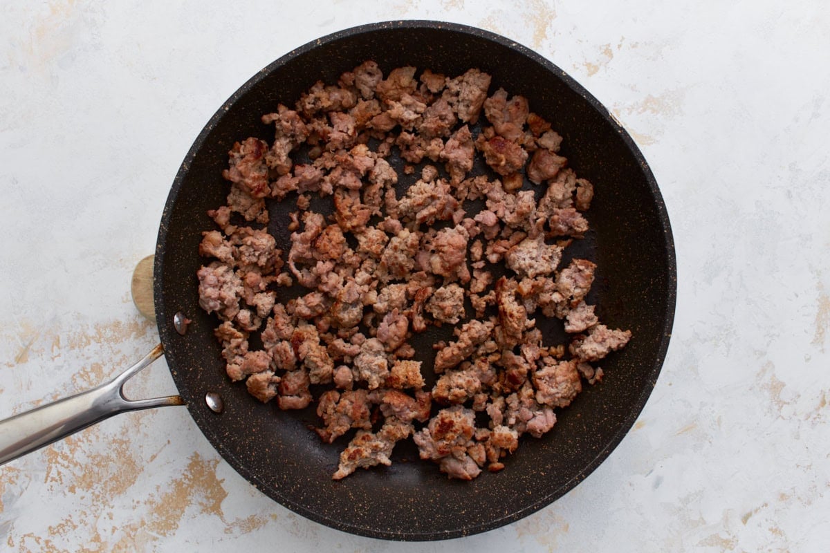 Crumbled breakfast sausage browning in a large nonstick skillet.