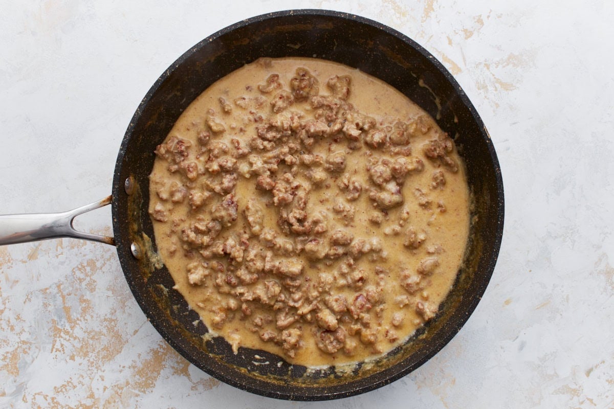 Cooked sausage in a rich, creamy gluten-free gravy filling a black skillet.