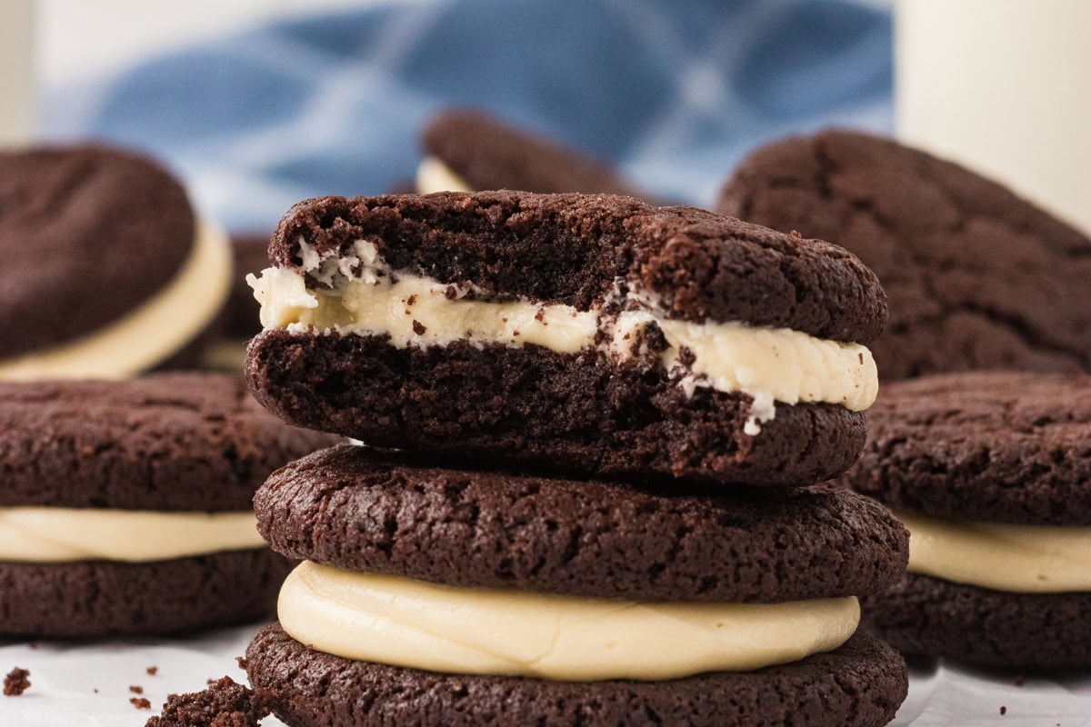 A bitten gluten free chocolate sandwich cookie stacked on top of other filled cookies, showing the soft texture and creamy vanilla marshmallow filling.