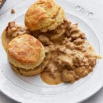 Two golden, fluffy gluten-free biscuits topped with creamy sausage gravy, served on a white plate.