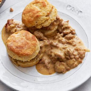 Two golden, fluffy gluten-free biscuits topped with creamy sausage gravy, served on a white plate.