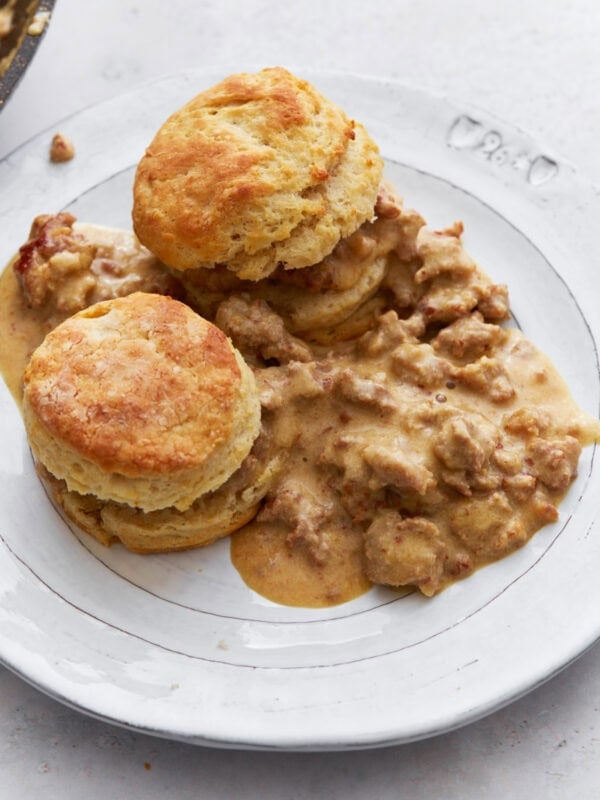 Two golden, fluffy gluten-free biscuits topped with creamy sausage gravy, served on a white plate.