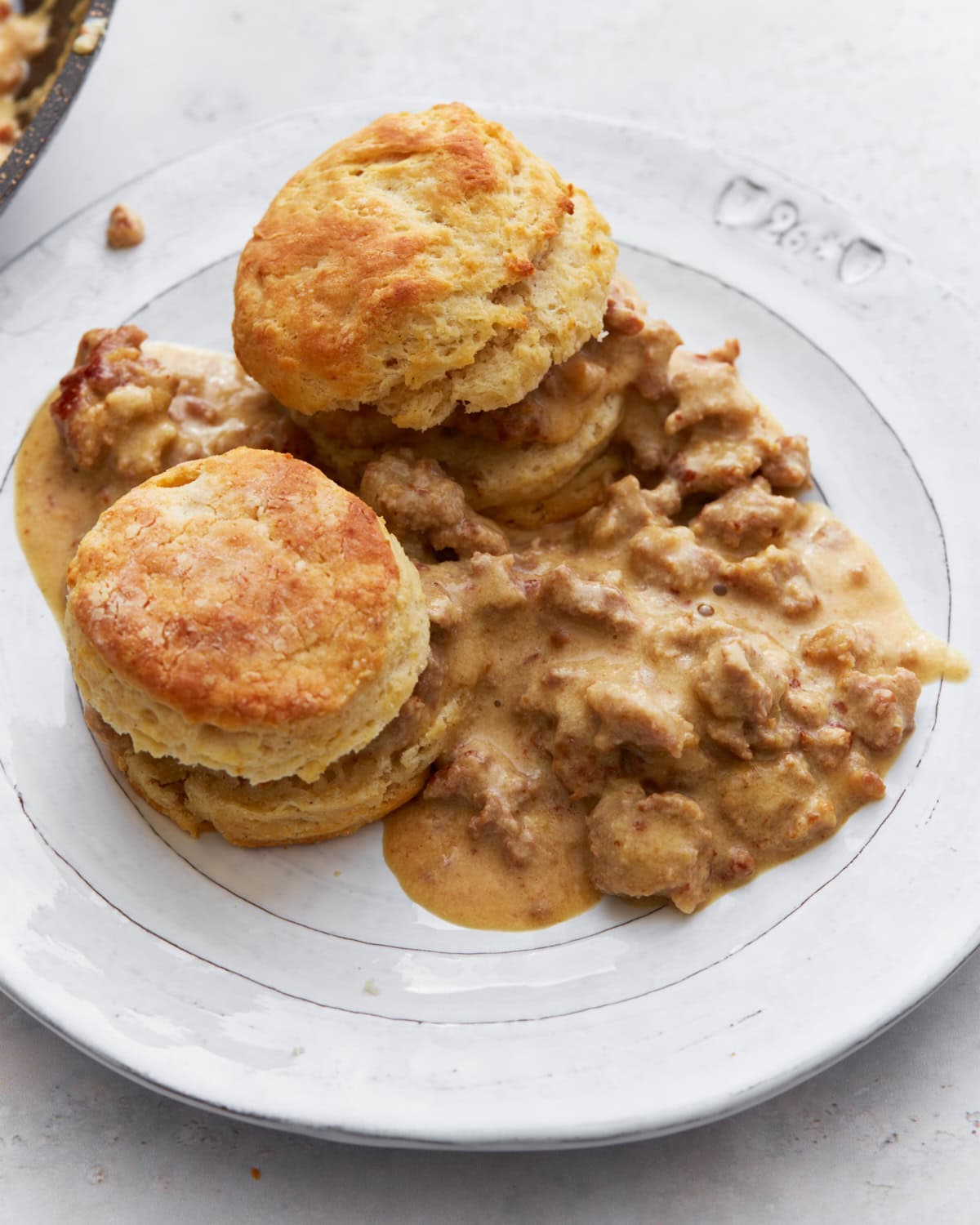Two golden, fluffy gluten-free biscuits topped with creamy sausage gravy, served on a white plate.