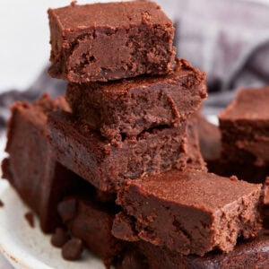 A stack of rich, fudgy keto brownies on a white plate, showing their dense, chocolatey texture with crispy edges.