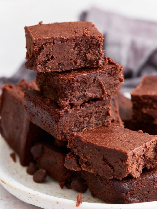 A stack of rich, fudgy keto brownies on a white plate, showing their dense, chocolatey texture with crispy edges.