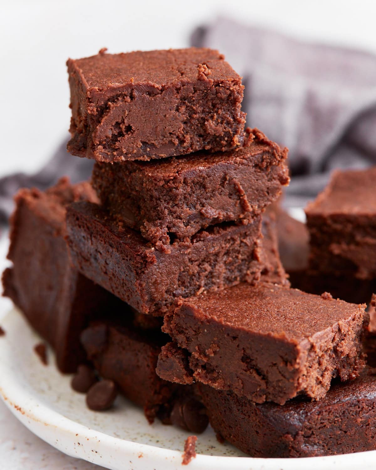 A stack of rich, fudgy keto brownies on a white plate, showing their dense, chocolatey texture with crispy edges.