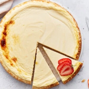 Whole baked keto cheesecake with one slice removed and garnished with fresh strawberry slices on a light background.