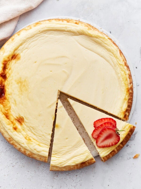 Whole baked keto cheesecake with one slice removed and garnished with fresh strawberry slices on a light background.