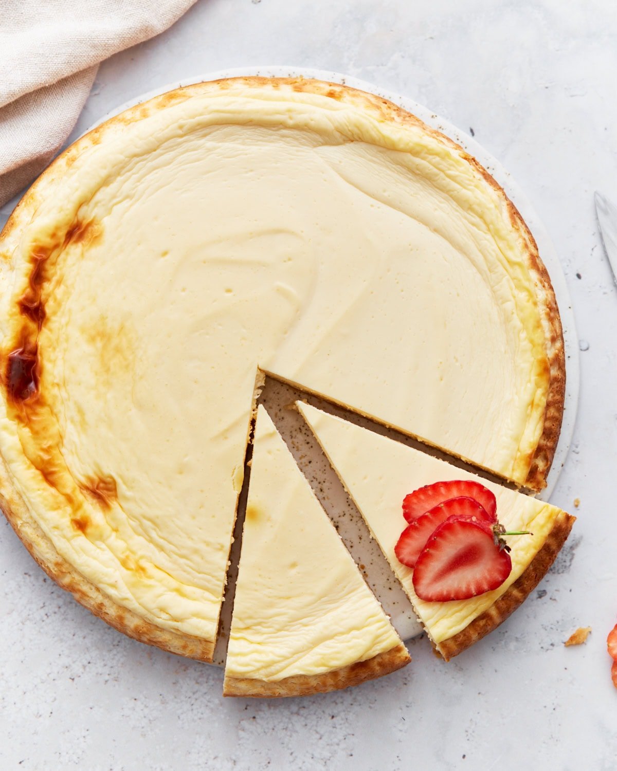 Whole baked keto cheesecake with one slice removed and garnished with fresh strawberry slices on a light background.