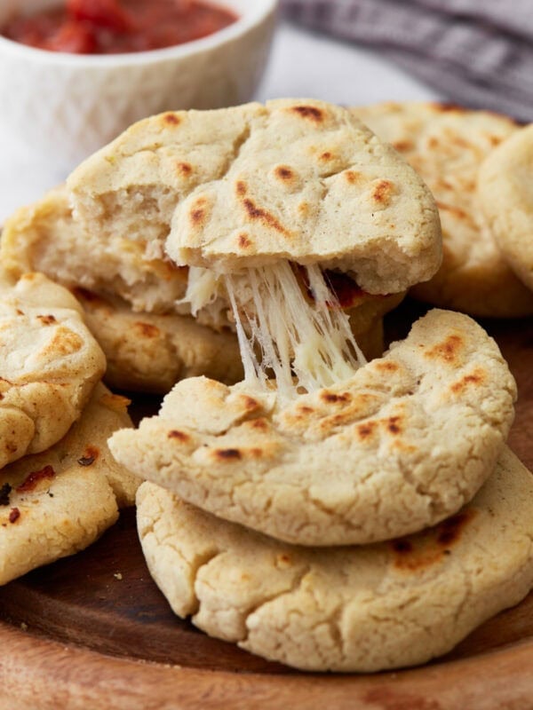 A plate of freshly cooked pupusas with golden brown spots, one torn open to show gooey melted cheese inside, with a bowl of salsa in the background.