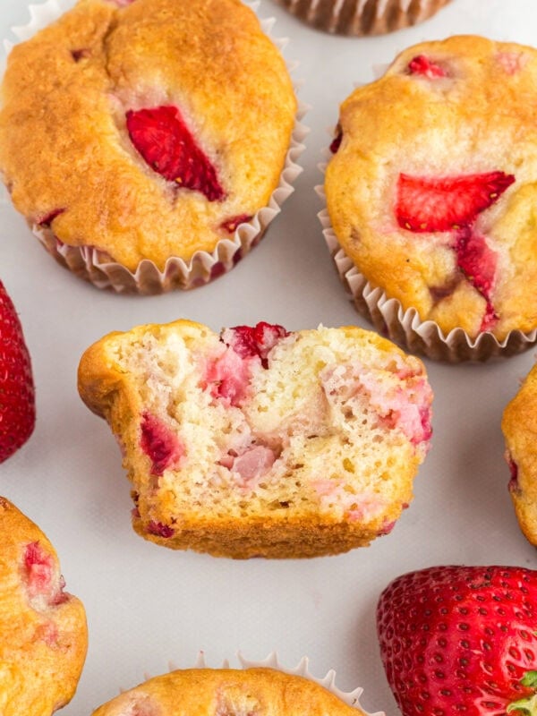 Gluten-free strawberry muffins with golden tops, one muffin cut in half to show the moist, fluffy crumb and chunks of fresh strawberries inside.