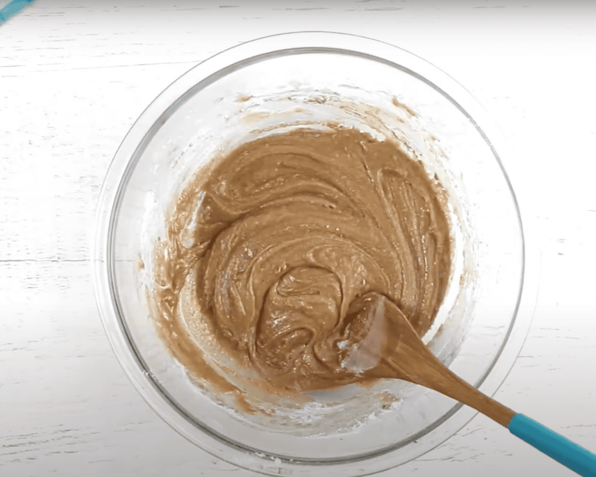 Gluten-free zucchini muffin batter partially mixed with a wooden spoon in a glass bowl.