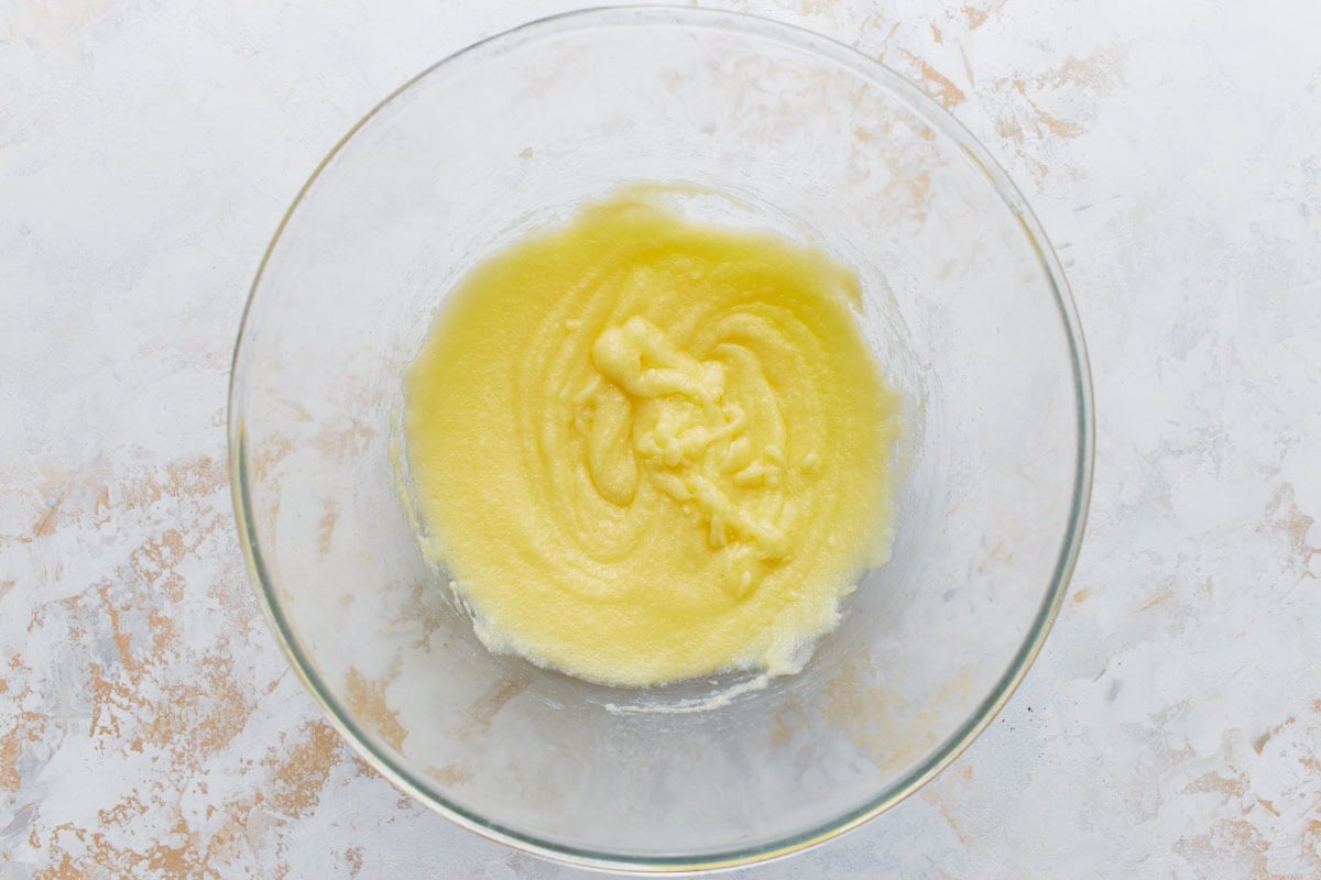 A glass bowl with melted butter and erythritol whisked together into a smooth yellow mixture.