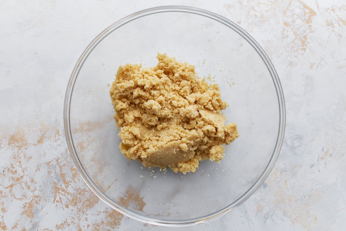 Crumbly almond flour crust dough mixture in a clear glass mixing bowl.