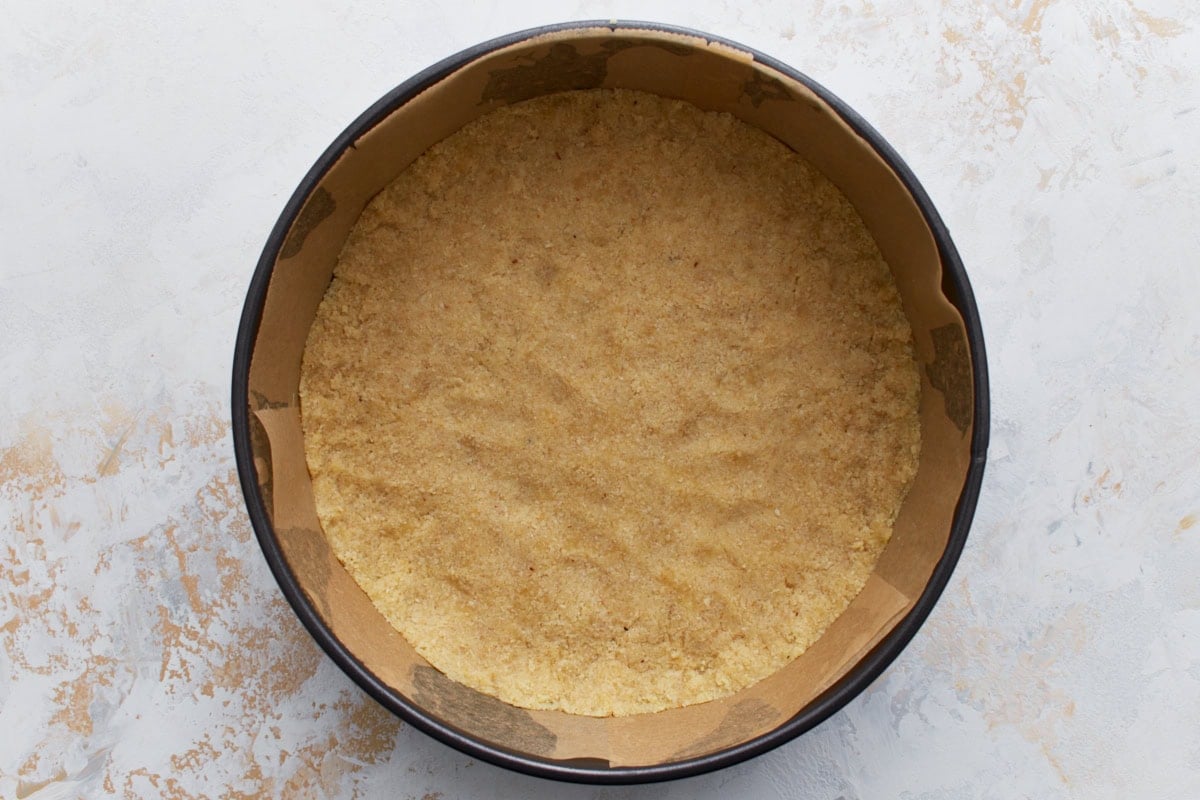 Unbaked almond flour crust pressed evenly into the bottom of a parchment-lined springform pan.