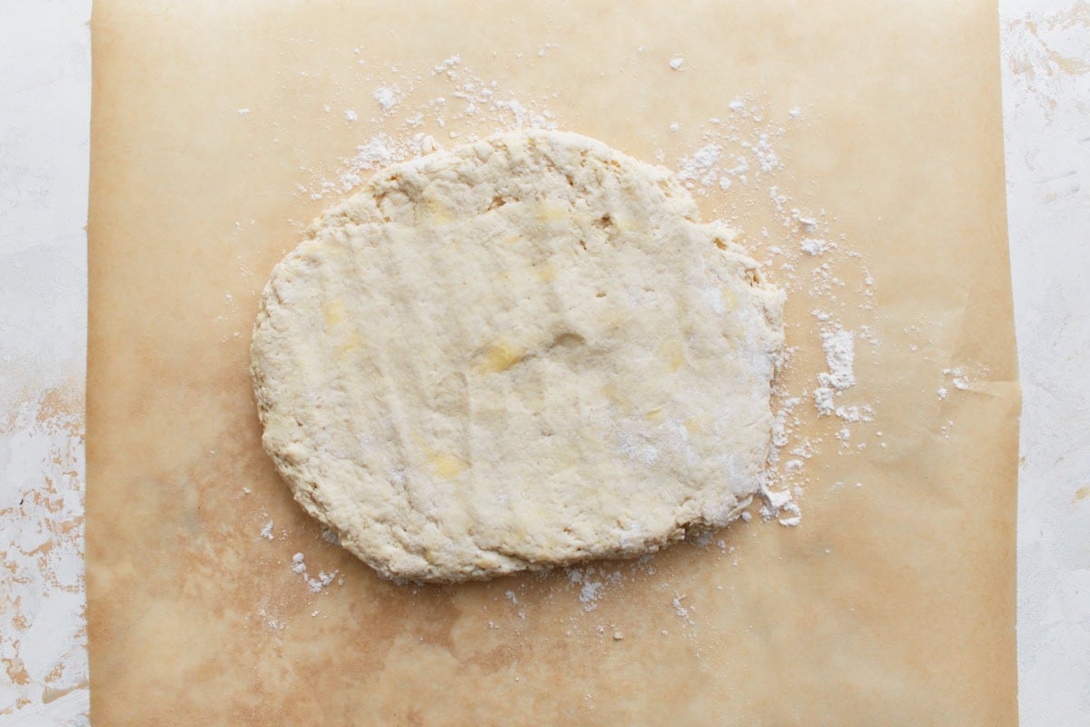 Gluten-free biscuit dough patted into a rough circle on floured parchment paper.