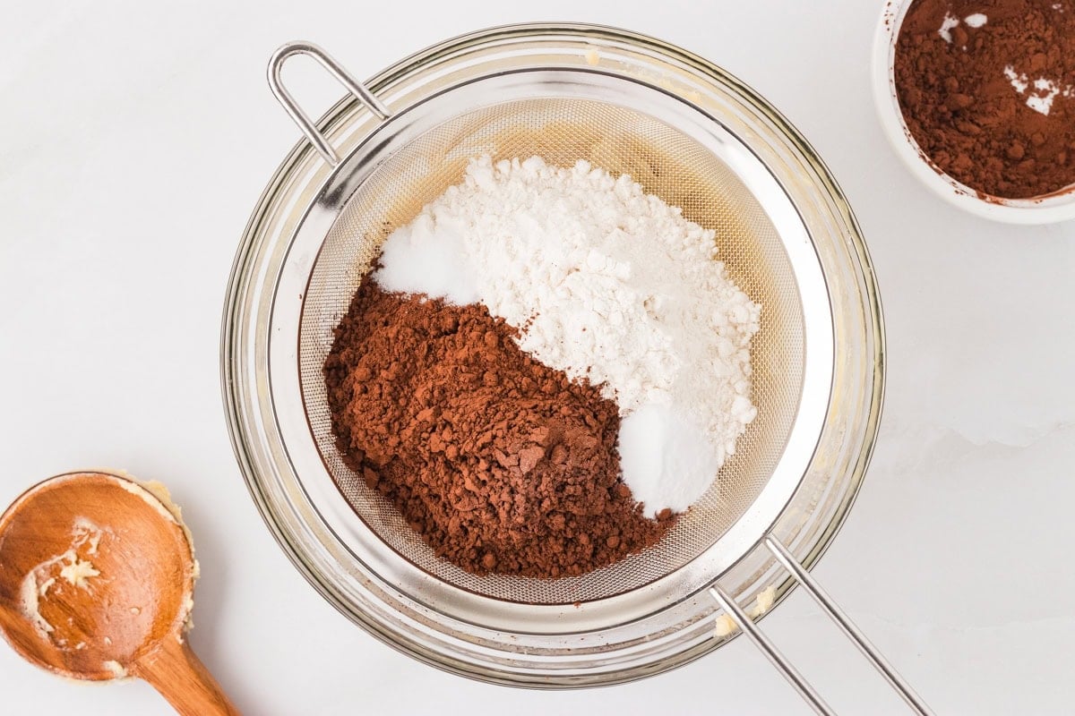 Gluten free flour, Dutch-processed cocoa powder, baking soda, and salt in a metal sifter set over a glass bowl.