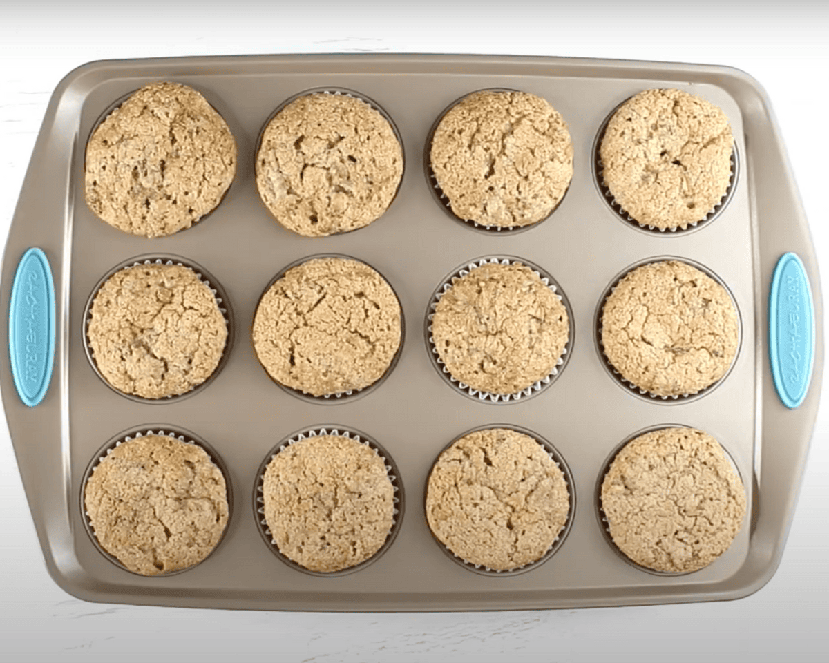 Freshly baked gluten-free zucchini muffins in a 12-cup muffin tin, golden and slightly cracked on top.