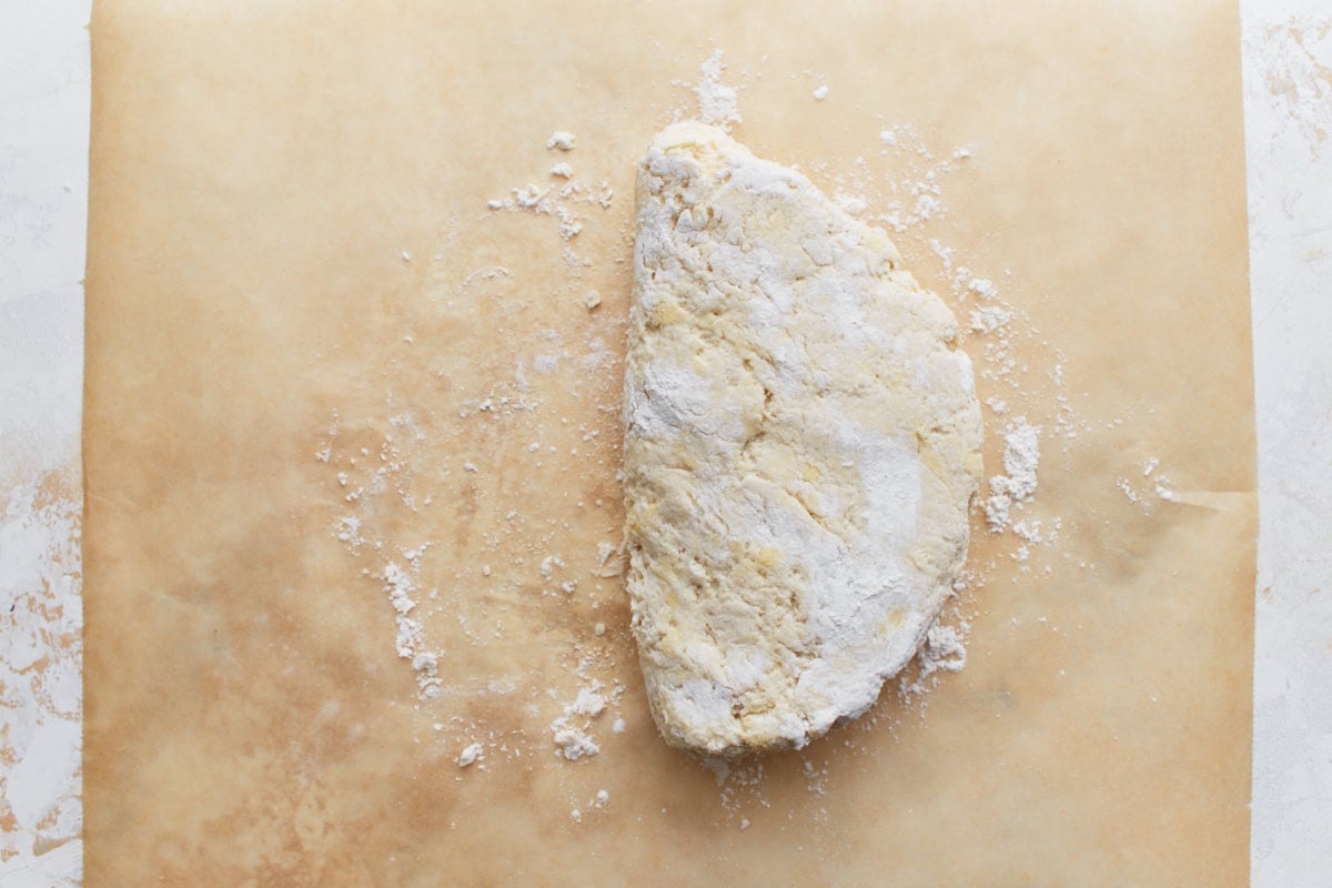 The biscuit dough folded in half on parchment paper, dusted with flour.