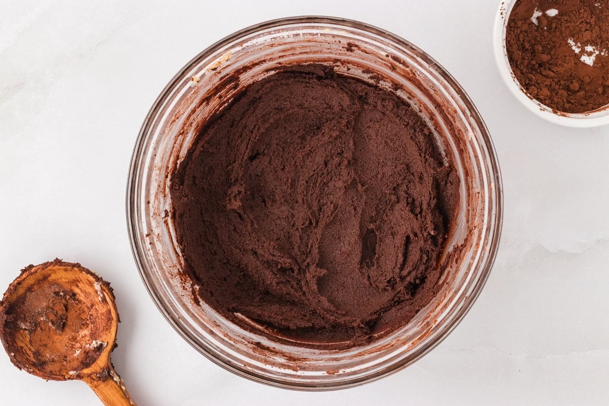 Fully mixed chocolate cookie dough with a rich dark color in a glass bowl, ready to be portioned.