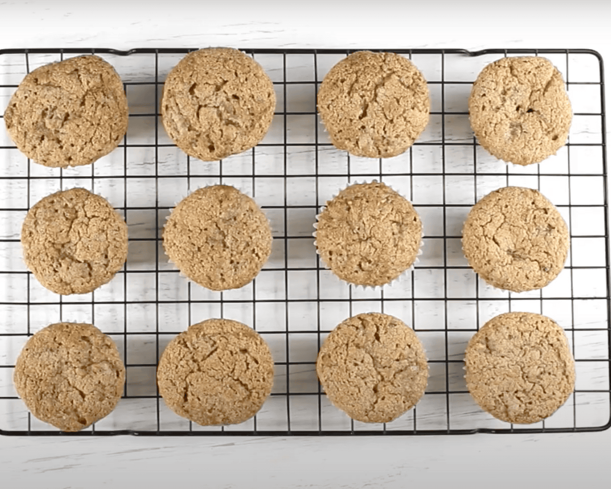 Baked muffins cooling on a black wire rack, evenly spaced and golden brown.