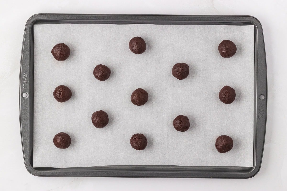 Portioned chocolate cookie dough balls evenly spaced on a parchment-lined baking sheet before baking.