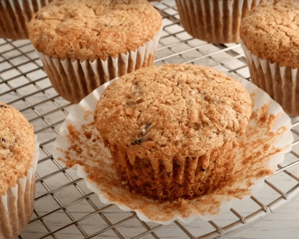Close-up of a gluten-free zucchini muffin on a wire rack with the wrapper peeled down, showing its moist texture and bits of shredded zucchini.
