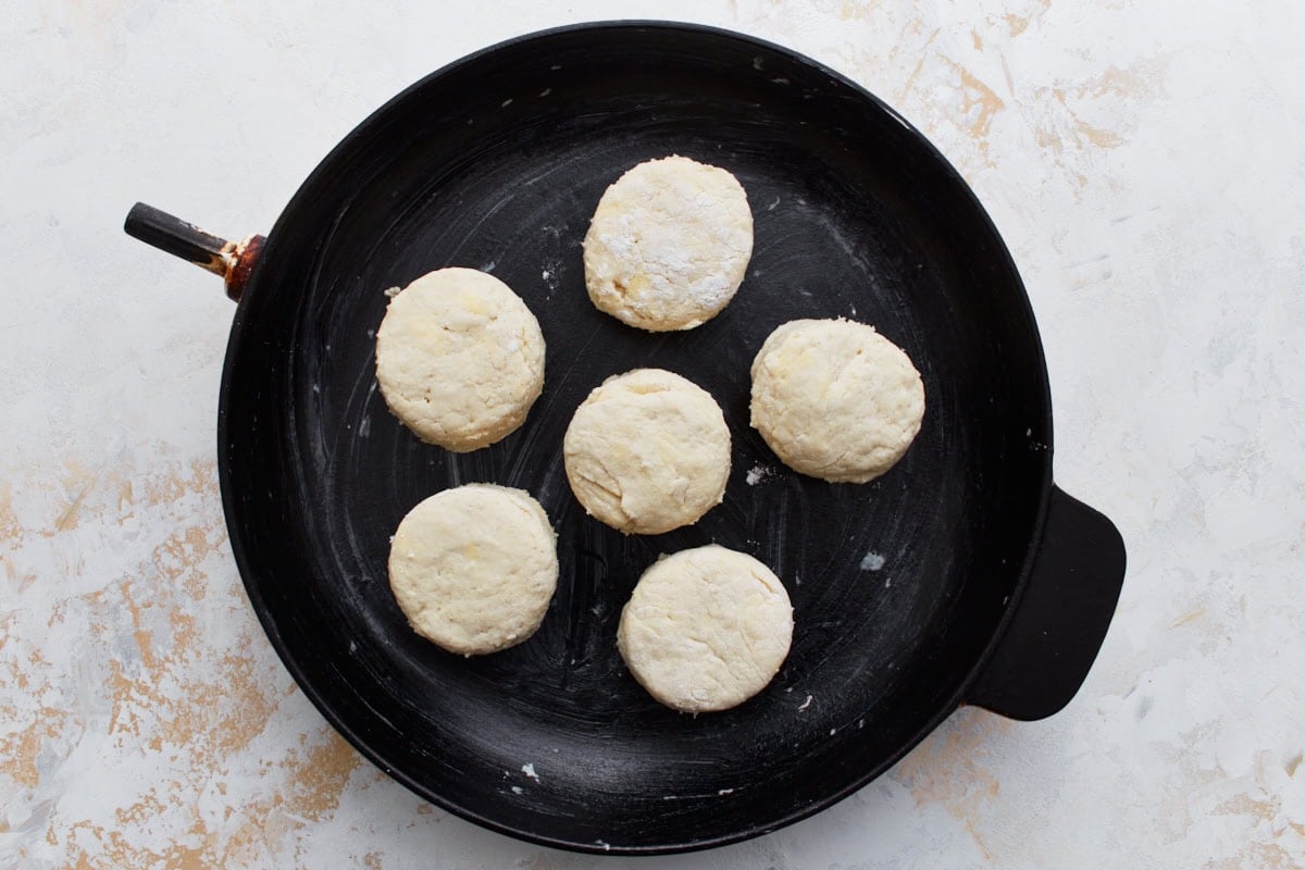 Six unbaked gluten-free biscuits placed in a greased black cast iron skillet.