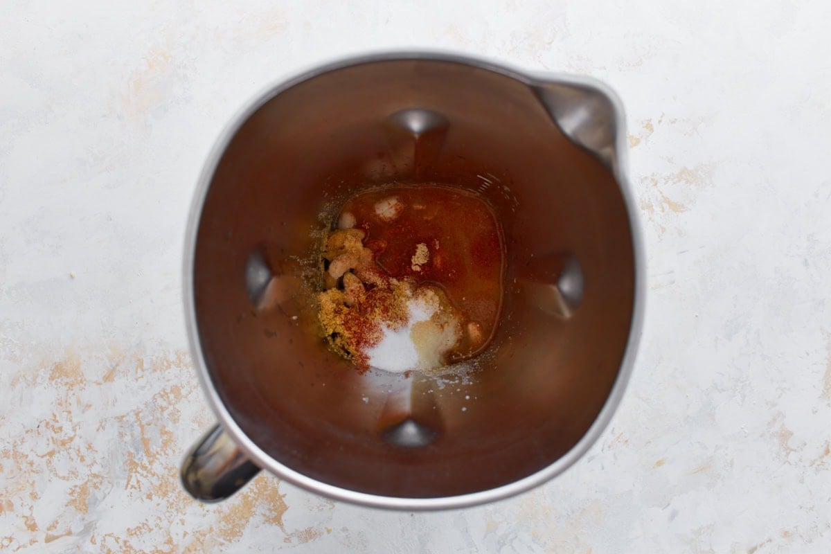 Top-down view of a blender filled with raw cashews, spices, nutritional yeast, and liquid ingredients before blending.